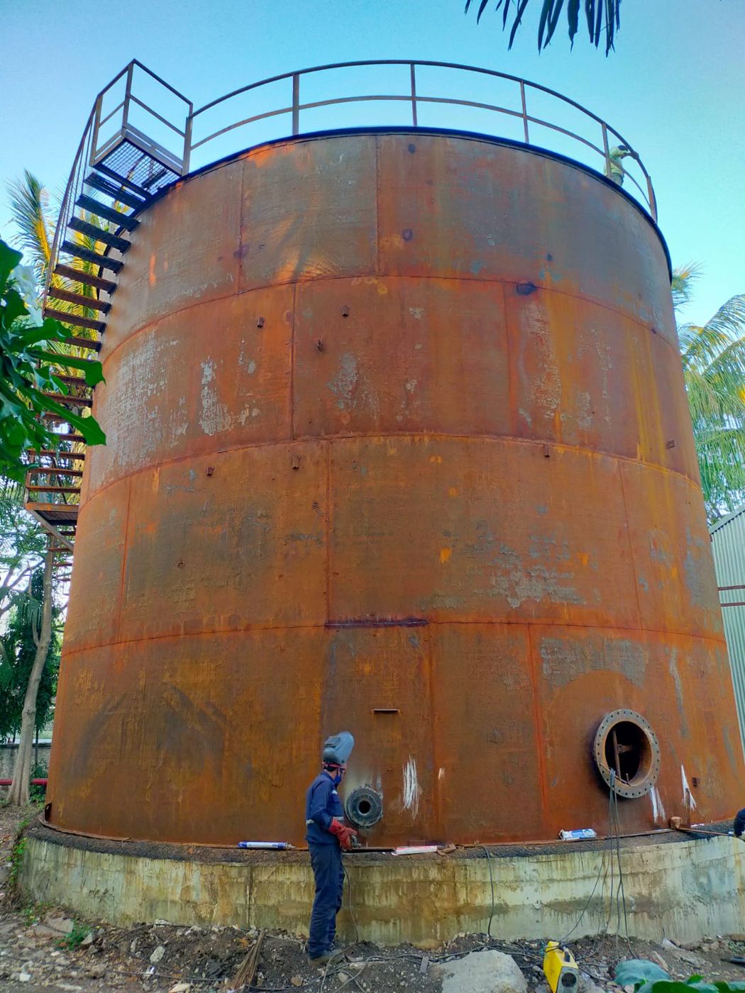 Welder working on nozzles of a large field storage tank